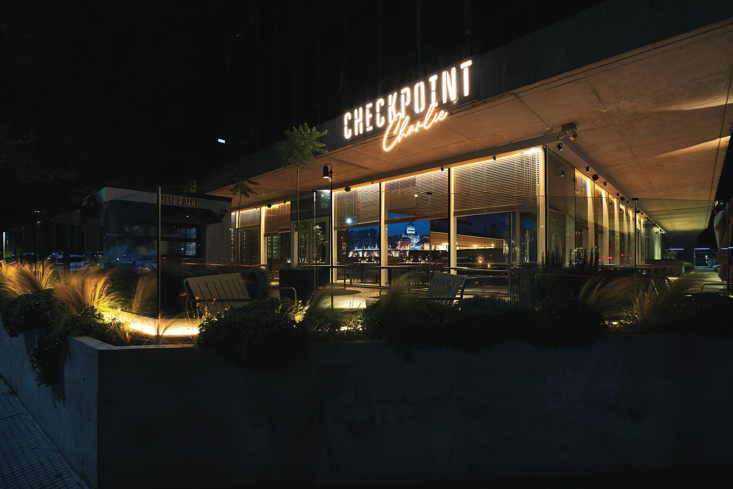 Fachada de Checkpoint Charlie de noche, con el cartel de neón encendido sobre la terraza